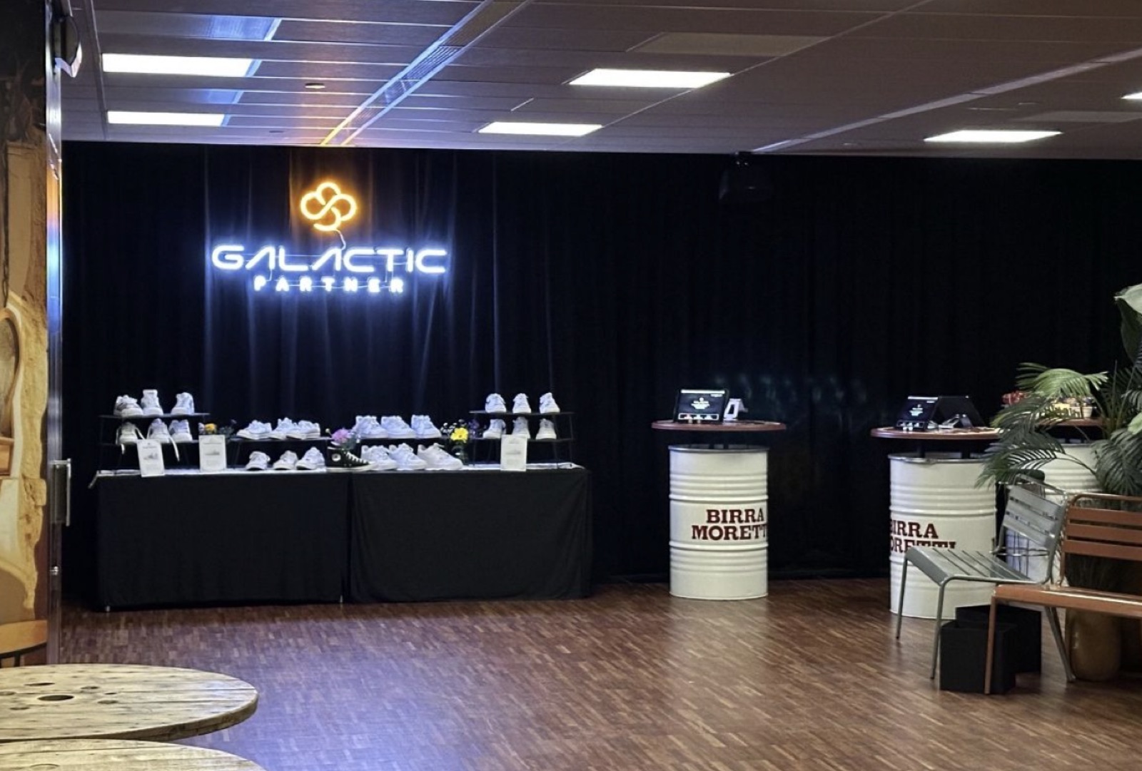 A lounge at a Beyond event branded Galactic Partner in neon, with the Galactic tier symbol above a table of sneakers.