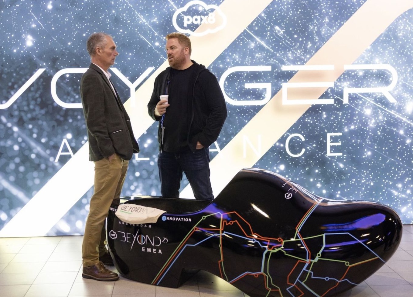 Two people talking at the Voyager Alliance booth at Beyond 2025, in front of a large Voyager Alliance sign.
